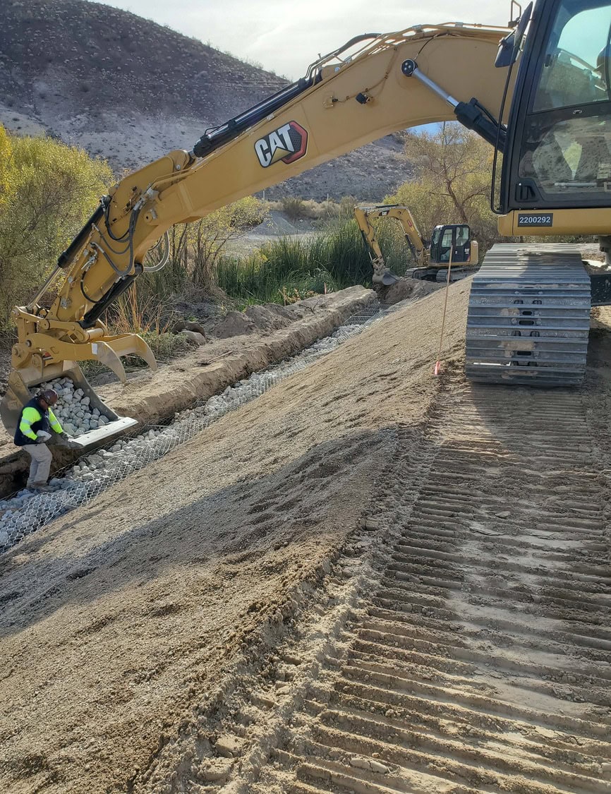 Excavator being used to install erosion control material along a sloped area during Scotty's Castle Flood Recovery.