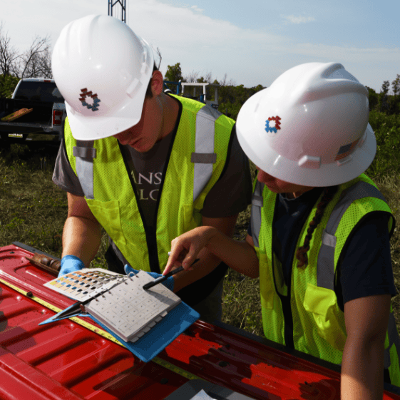 Tepa Companies' workers in high-visibility safety vests and hard hats examining a chart for soil and material analysis.